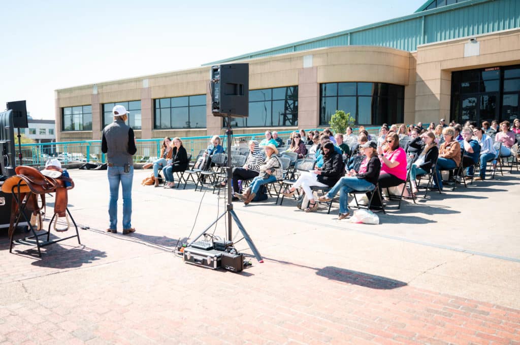 a speaker addressing a seated audience outdoors near a building under clear skies.