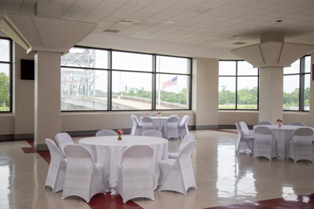 3 round tables with chairs around it. all are covered in white tablecloth. the background has a bridge and american flag