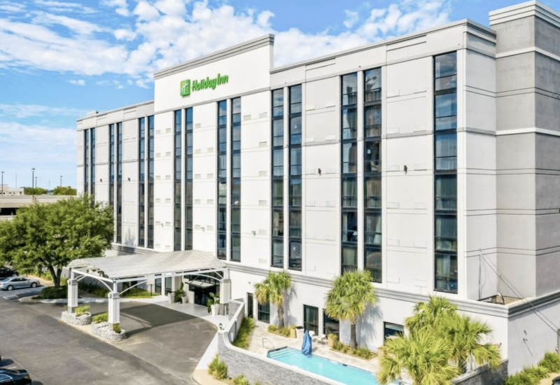 a Holiday Inn building with a white facade, large windows, and palm trees.